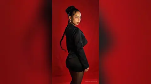 Elegant woman in a black satin blazer posing against a bold red background for a sophisticated fashion portrait.