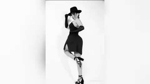 Elegant woman in a black cocktail dress, lace gloves, and wide-brimmed hat posing against a white studio background.