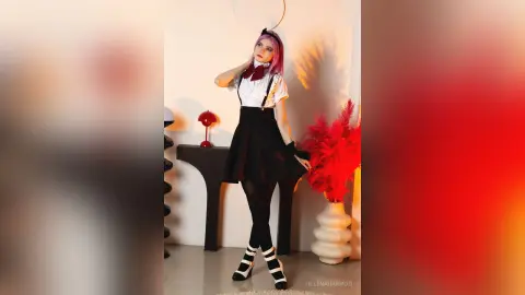 Pink-haired woman in a white blouse and black skirt posing in a warm, moody studio setting.
