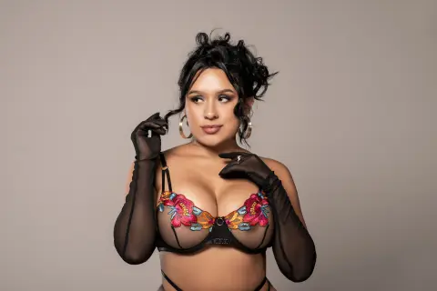 Beautiful woman in floral lace lingerie and long black gloves posing against a neutral studio background.