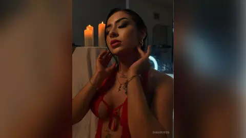Glamorous woman in a red lace outfit posing by candlelight in a moody, romantic setting.