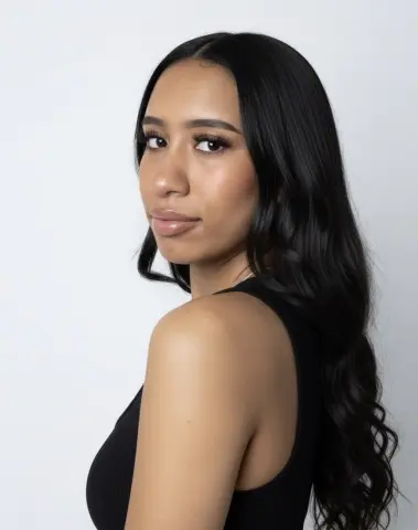 Young woman with long wavy black hair wearing a black sleeveless top against a white background.