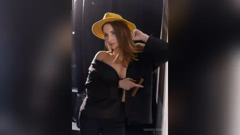 Stylish woman in a black blazer and yellow wide-brimmed hat posing with a confident, chic mood.