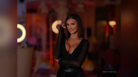 Glamorous woman in a black long-sleeve dress posing in a warm, dimly lit evening setting.
