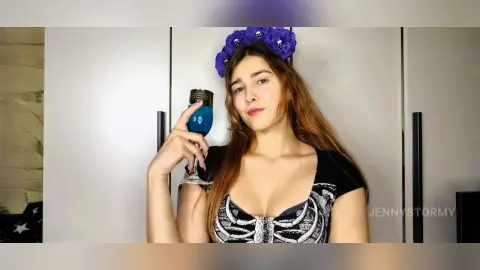 Young woman in a black corset and purple flower crown holding a blue drink in a bright indoor setting.