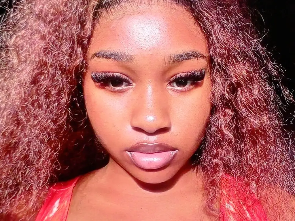 Close-up portrait of a beautiful Black woman with voluminous curly red hair and glamorous makeup.