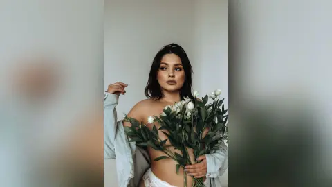 Elegant woman in a light blue shirt holding a bouquet of white flowers in a minimalist indoor setting.