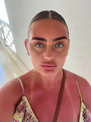 Bellamay95 looks directly at the camera with her hair slicked back, wearing a floral patterned camisole with thin straps.