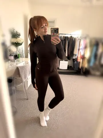 GingerXSpiceUK poses in a mirror wearing a tight black long-sleeve top and matching leggings with white socks.