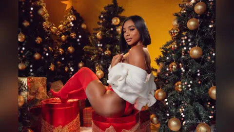 Beautiful woman in a white sweater and red outfit sitting on gift boxes near festive Christmas trees.