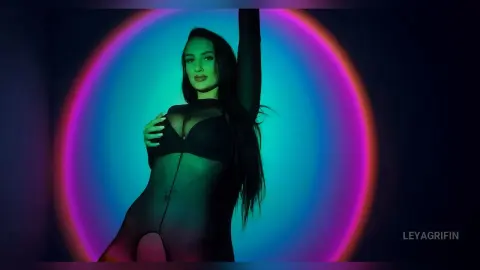 Moody portrait of a woman in black sheer lingerie against a vibrant neon pink and blue circular light background.