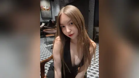 Young woman in a black sleeveless dress smiling in a modern cafe with checkered flooring.