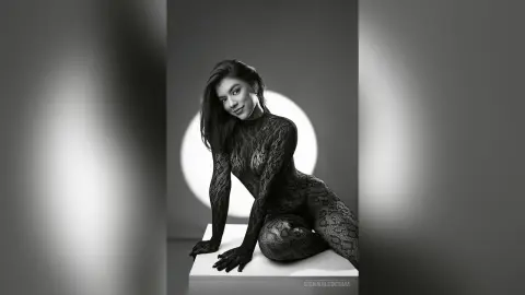 Elegant woman in a black lace bodysuit posing against a minimalist studio backdrop in moody black and white.
