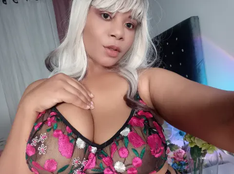 Woman with silver hair wearing a floral pink mesh bralette in a cozy bedroom setting.