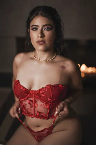 Young woman in red lace lingerie posing in a moody, dimly lit indoor setting.