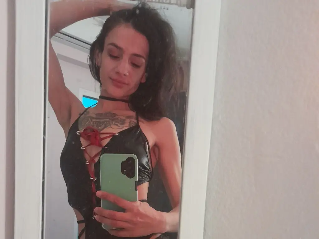 RebeccaStronge poses for a mirror selfie wearing a black lace-up top that shows her chest tattoos and dark hair.