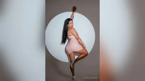 Woman in a pink satin mini dress posing elegantly against a white circular backdrop in a studio setting.
