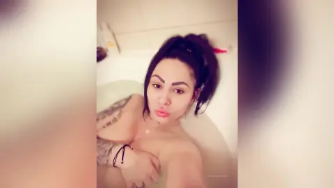 DeeaAnderson poses naked in a white bathtub, looking at the camera with her dark hair pulled back.