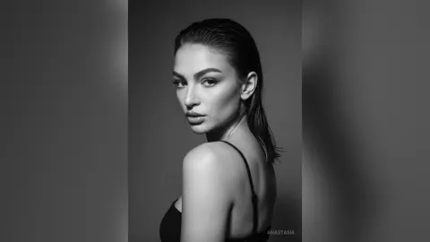 Elegant woman in a black strap top posing for a moody black and white studio portrait.