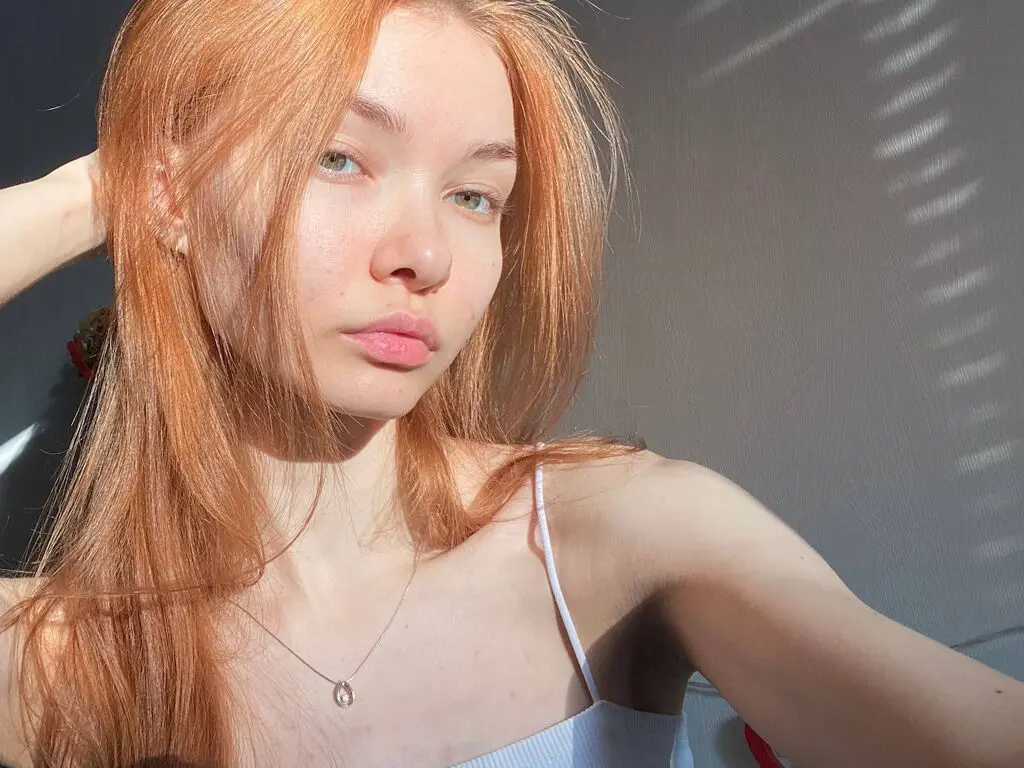 Redheaded woman in a white camisole posing in warm sunlight for a soft, natural portrait.