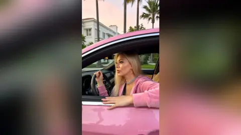 Blonde woman in a pink velvet top sitting in a pink car near palm trees during a sunny day.