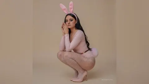 MiaAngelove — MiaAngelove wears a pink bunny outfit with ears and fishnet tights while crouching in a studio.