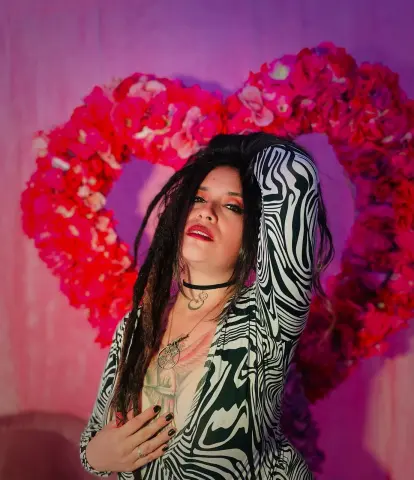 Woman in black and white zebra print dress posing before a large pink floral heart backdrop.