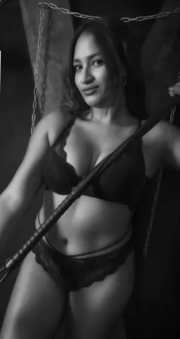 Shantal_slav poses in black lace lingerie while holding a dark pole against a dark background.