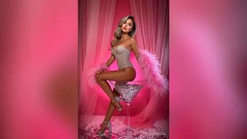 Glamorous woman in a sparkling silver bodysuit and pink feather cuffs posing against a pink backdrop.
