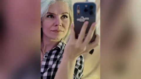 LeyaTaryn takes a mirror selfie wearing a black and white plaid shirt.