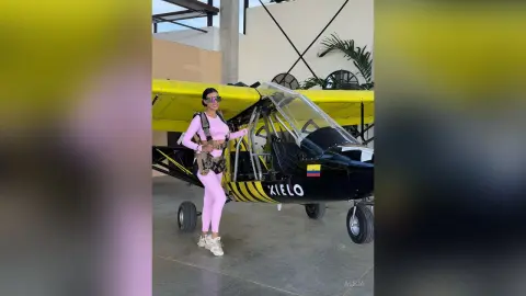 Aleja stands next to a black and yellow light aircraft wearing a pink long-sleeve crop top and matching pink leggings.