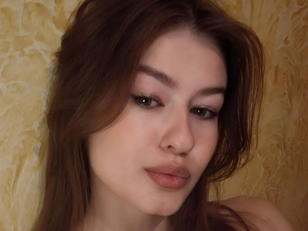 KarenFalknar looks into the camera with her long brown hair framing her face against a textured yellow wall.
