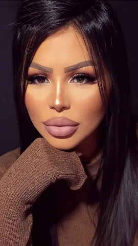 Close-up portrait of a woman with long dark hair and glamorous makeup wearing a cozy brown ribbed sweater.