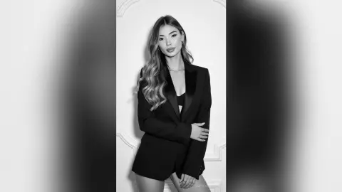 Elegant woman in a black blazer and bra top posing against a white wall in a sophisticated studio setting.