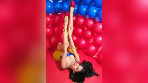 JessieLiu lies on a red floor with her legs raised high, wearing a blue bikini top and yellow bottoms.