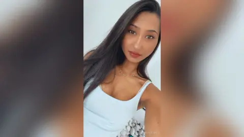 Young woman in a white tank top smiling against a plain white background for a clean lifestyle portrait.