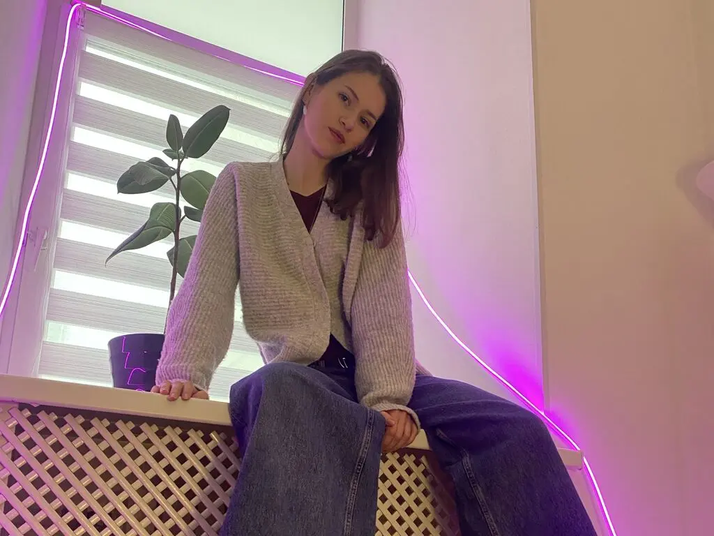 Young woman in a white satin blouse and black trousers posing elegantly against a neutral studio background.
