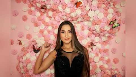Elegant woman in a black sleeveless dress posing against a romantic pink rose wall with butterflies.