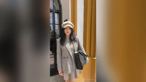 Stylish woman in a grey plaid blazer and beige beret standing by a doorway in a chic urban setting.
