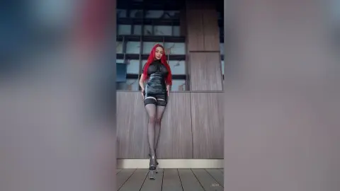 Red-haired woman in a sleek black mini dress posing on a modern wooden balcony with a moody atmosphere.