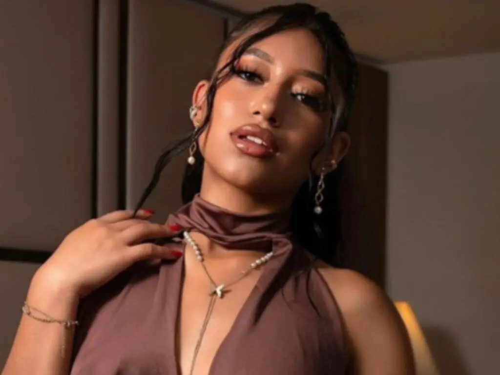 AmbarReed poses in a brown halter top, showing her face, neck, and shoulders with long dark hair and jewelry.