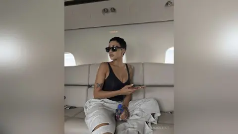 Stylish woman in black tank top and grey sweatpants relaxing on a luxury private jet seat.