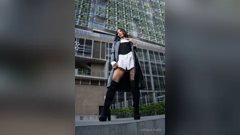 Stylish woman in a white shirt, black shorts, and tall boots posing confidently against a modern city building.