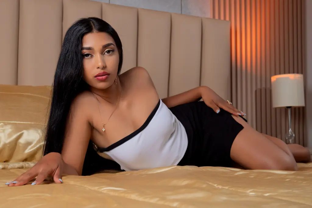 JasminMale — JasminMale lies on a gold bed wearing a white tube top and black shorts, posing with her long black hair down.