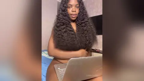 Young woman with long wavy hair sitting in a bedroom near a laptop in a relaxed mood.