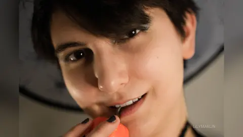 Close-up portrait of a smiling young woman with dark hair in a soft, natural indoor setting.