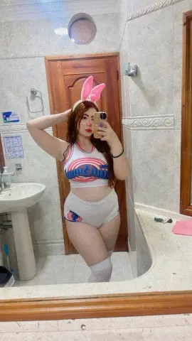 Young woman in a red and white crop top and white shorts wearing bunny ears in a bathroom mirror selfie.