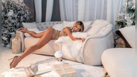 Glamorous woman in a gold sequin outfit lounging on a white sofa in a festive, snowy Christmas setting.