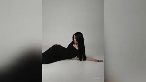 Elegant woman in a black evening dress posing gracefully against a minimalist white studio background.
