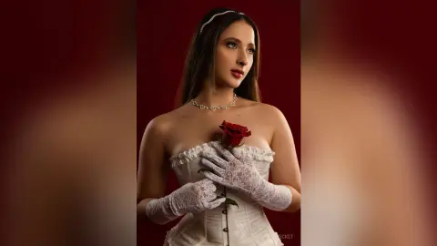 Elegant woman in white lace corset and gloves holding a red rose against a moody dark red background.
